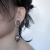 a woman's ear with a tiger skull silver earring inside a ear tunnel
