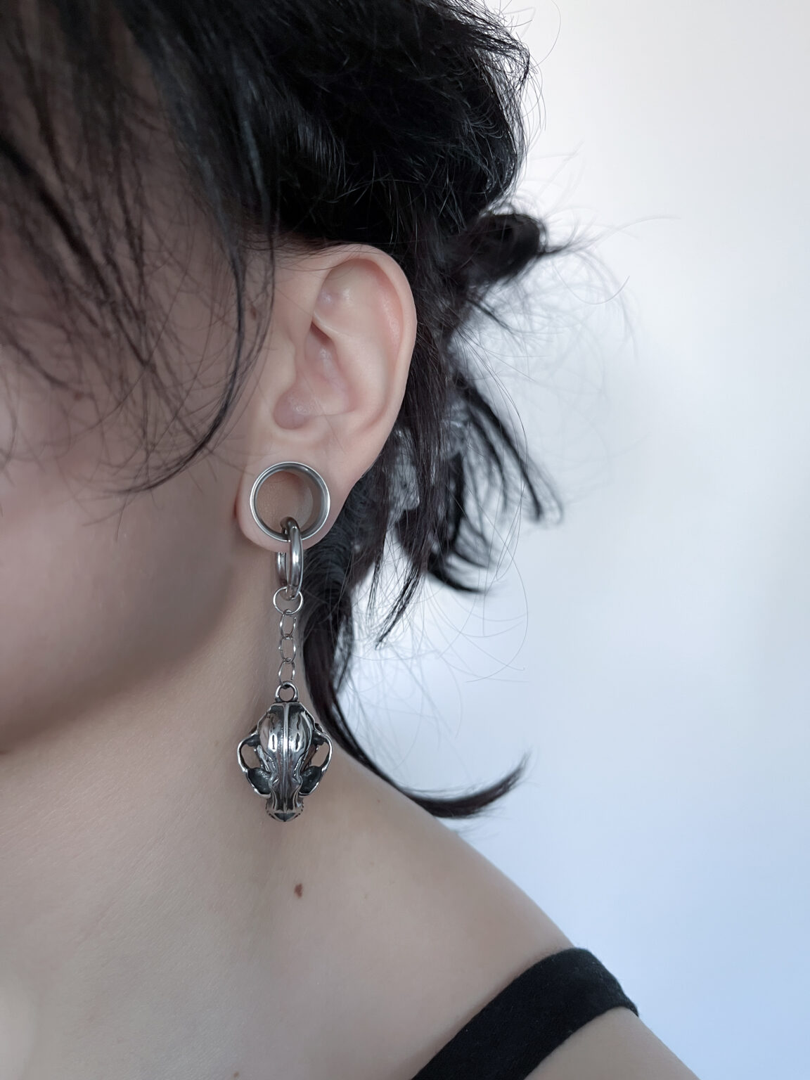 a woman's ear with a tiger skull silver earring inside a ear tunnel